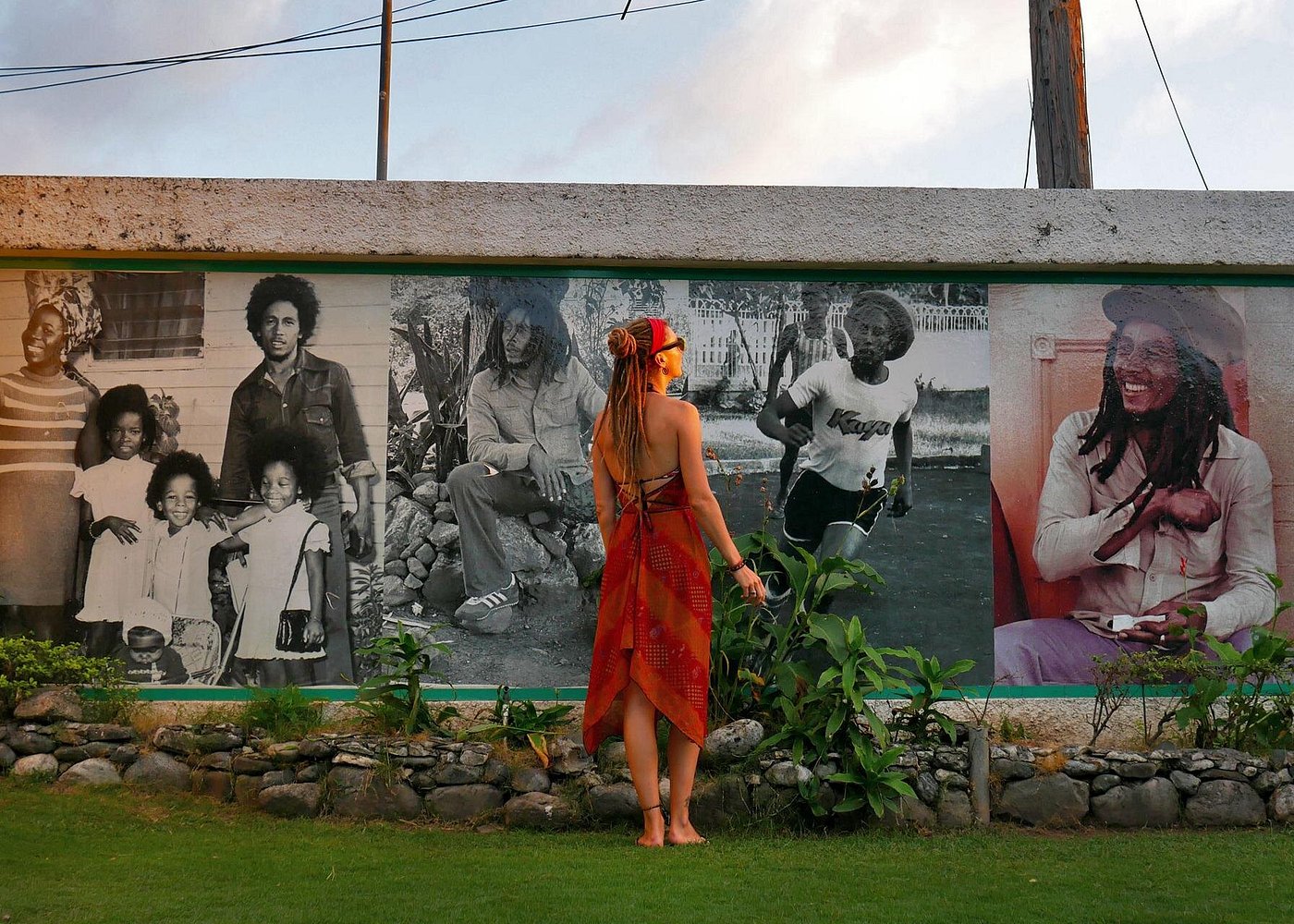 a woman standing in front of the Bob Marley museum with murals of Bob Marley painted on the building