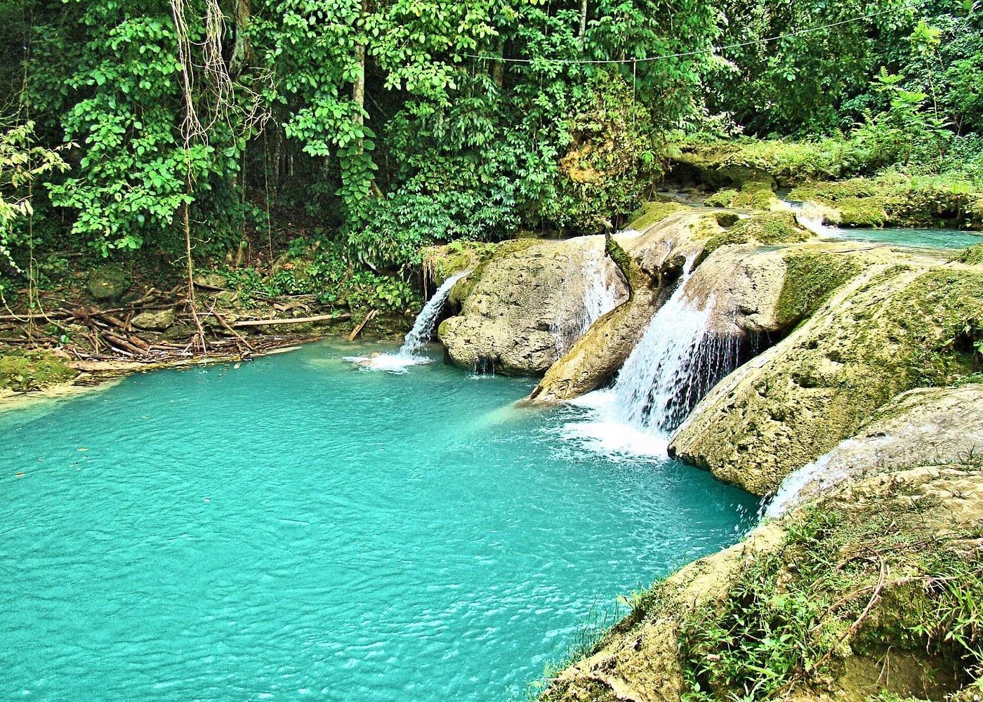an image of a waterfall cascading into a blue swimming hole surrounded by lush greenery