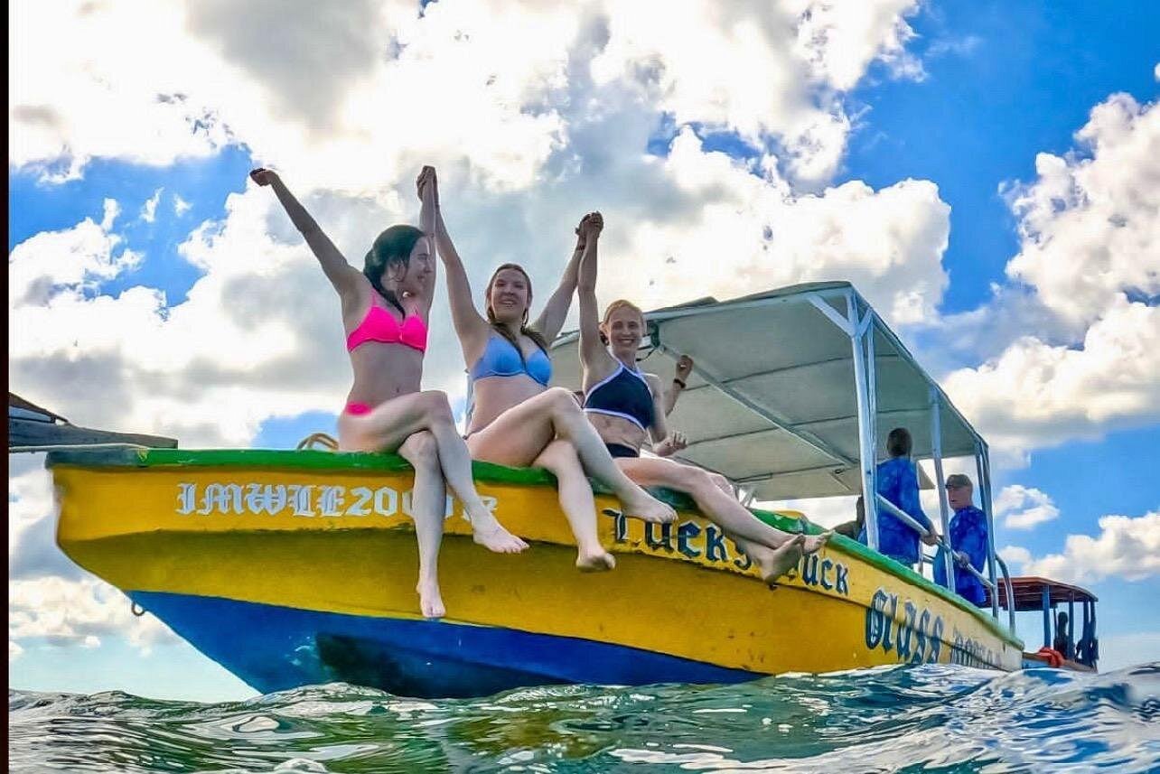 three people sitting on the edge of a glass bottom boat with their hands raised in the air having fun in jamaica