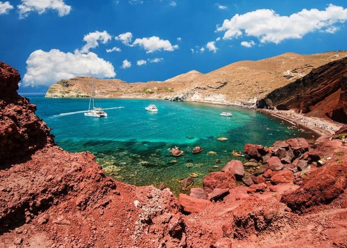 A narrow, pebbly Red Beach hemmed in by high scarlet cliffs and scattered with large volcanic rocks.